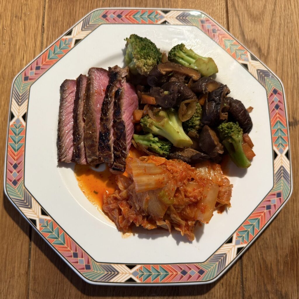 Teller rosa gebratenes Rindfleisch, diverse Gemüse und Kimchi