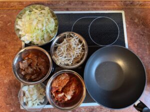 Vorbereitete Zutaten des Gerichts in Schüsseln auf dem Herd neben einem Wok